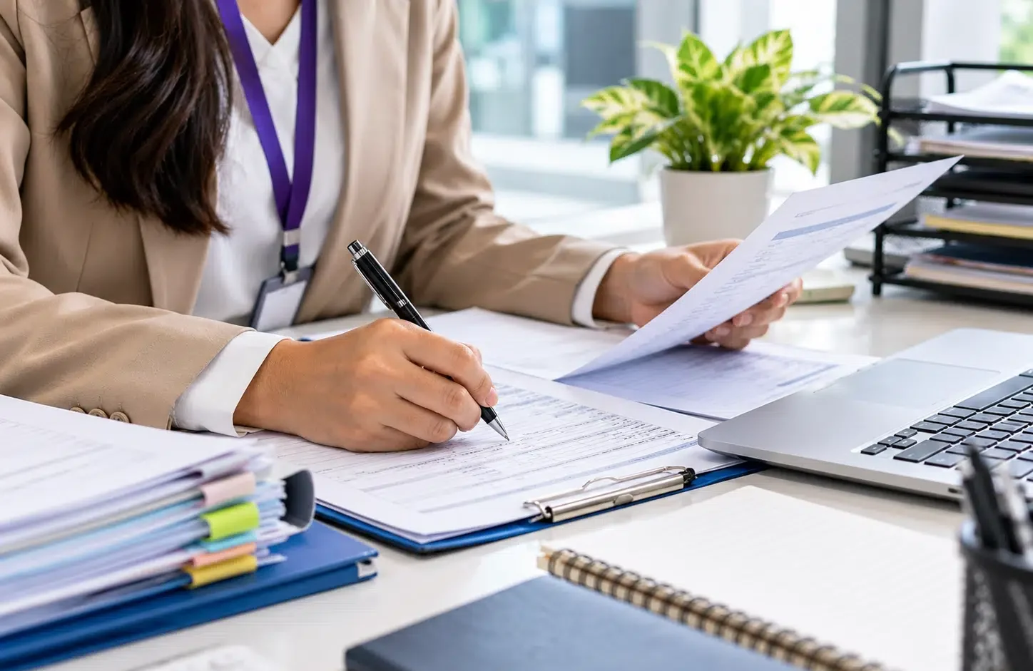 Business professional reviewing financial documents and completing administrative paperwork beside a laptop.