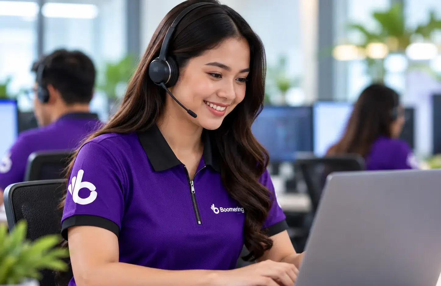 Boomering customer service specialist wearing a headset and assisting clients from a laptop in a modern office.